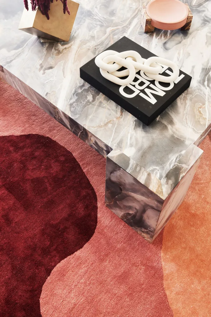 A red and orange rug underneath a coffee table with neutral tones