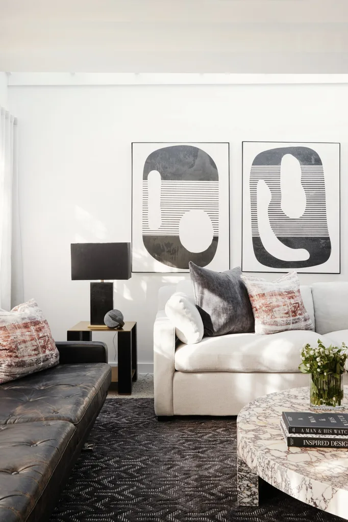 A modern style living room with a dark rug, black and white artworks, a dark leather couch, white couch and a marble coffee table that is white with dark toned veining.