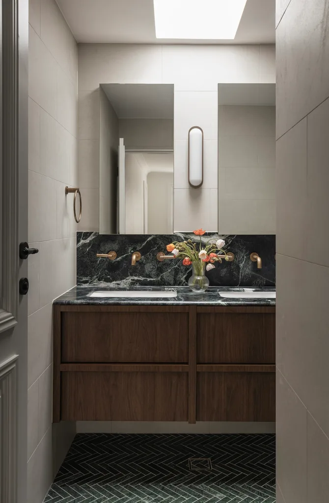 Neutral bathroom featuring walnut drawers, a marble vanity and green tiled floor, plus a wall light