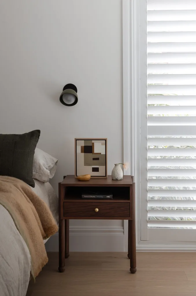 Neutral earthy bedroom with a timber bedside table and plantation shutters