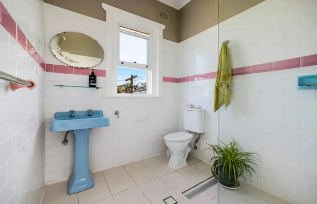 Retro bathroom with white and pink subway tiles and blue pedestal sink and green wall paint