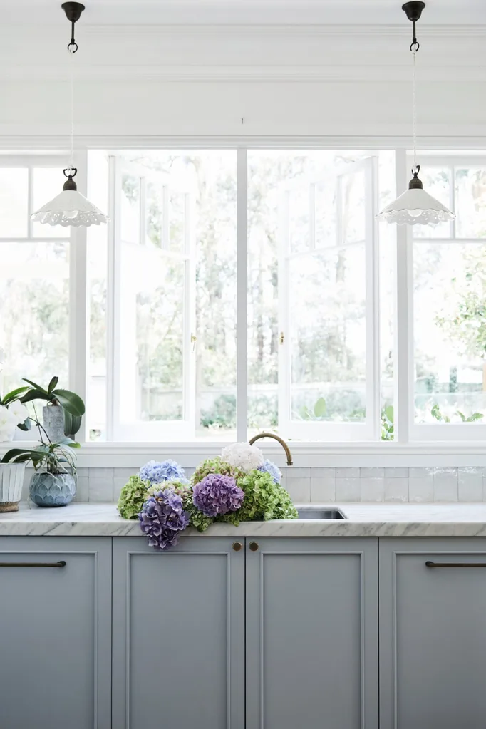 alexandra nea's kitchen sink with grey joinery, pendant lights, a carrara marble benchtop and hydrangeas