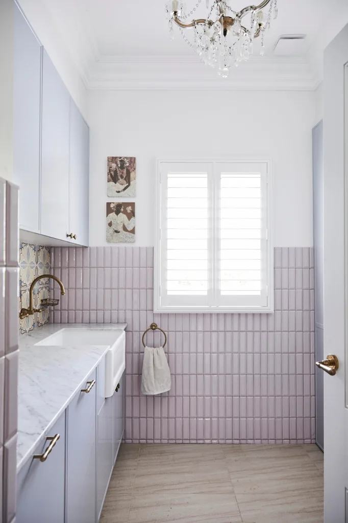 alexandra nea's laundry featuring pink tiles, plantation shutters, a marble benchtop farmhouse sink and brass tapware