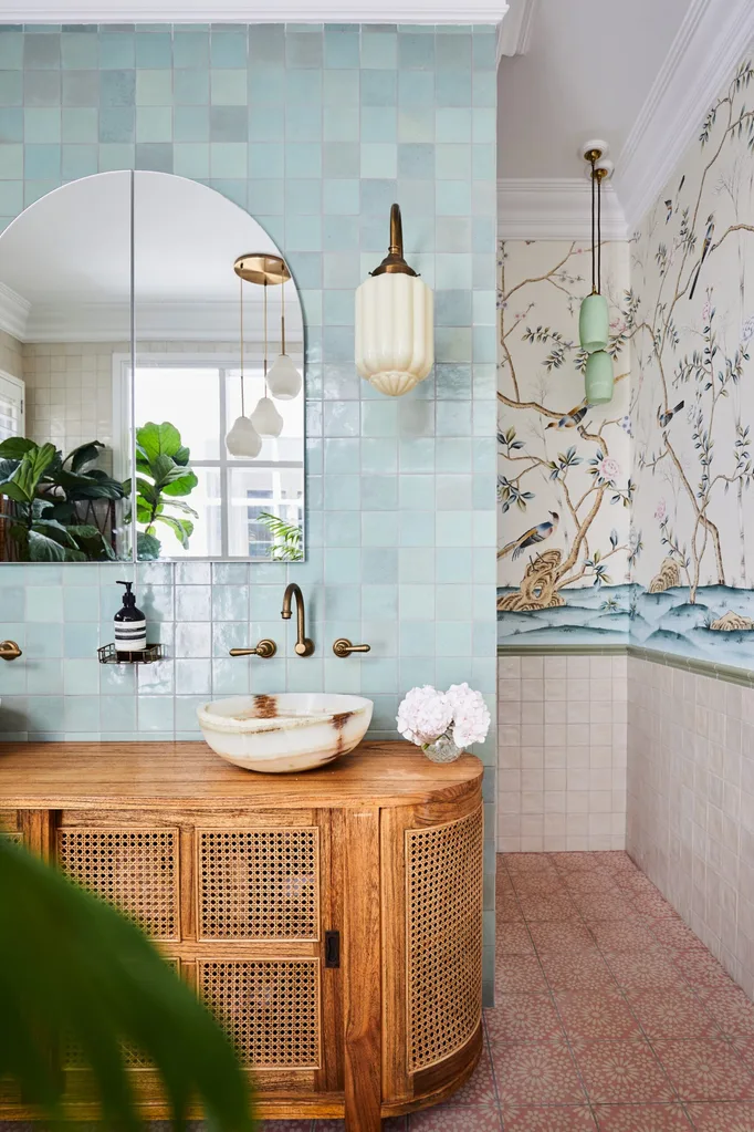alexandra nea's main bathroom featuring a rattan timber vanity, blue zellige tiles, a vintage brass wall light and arched mirror, plus botanical wallpaper