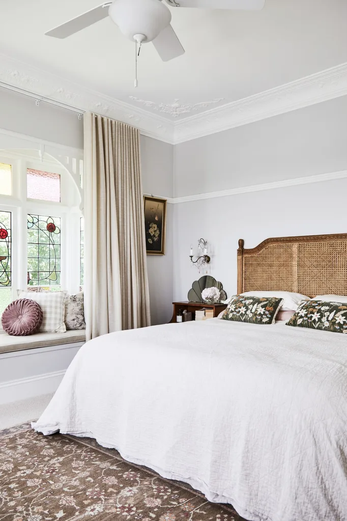 alexandra nea's main bedroom featuring a rattan bedhead, antique wall sconces, leadlight windows, grey walls and adairs linen