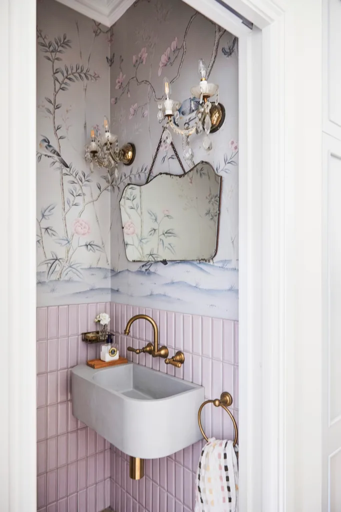 alexandra nea's powder room featuring pink tiles, floral wallpaper, a vintage mirror, brass tapware and a wall-hung sink, plus antique wall lights