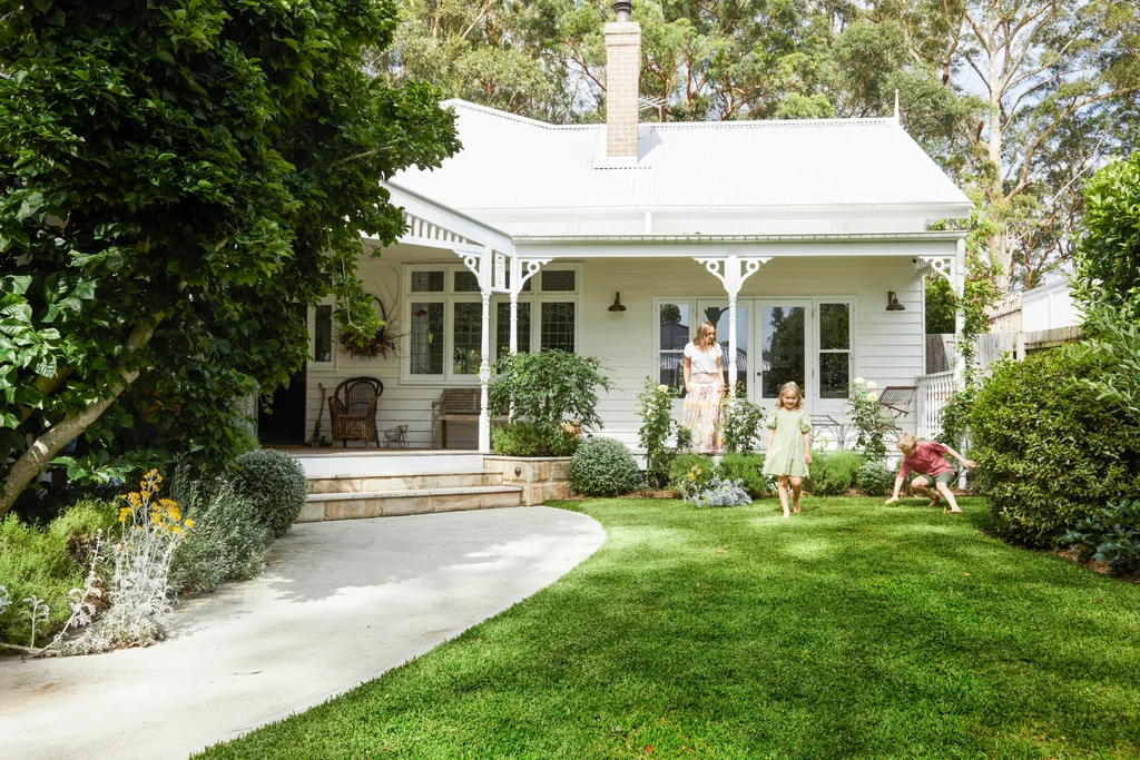 alexandra nea's white weatherboard house with a colorbond roof and fretwork, with a lawn, driveway and garden in front.