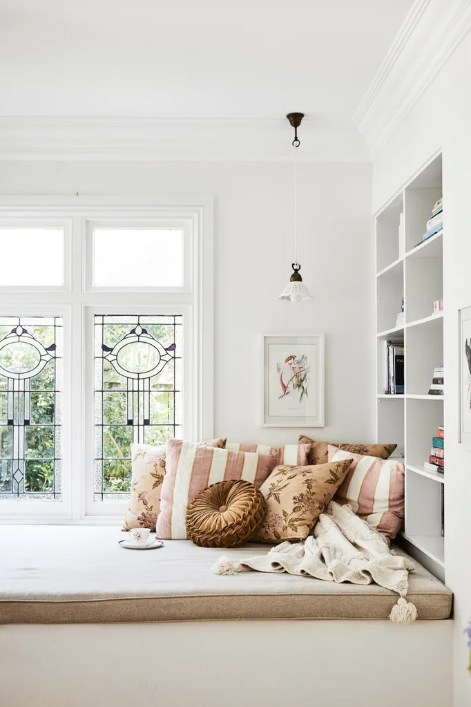 alexandra nea's window seat daybed with striped cushions, leadlight windows, white walls and a built-in bookshelf