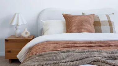 white organic curved bed frame with a white duvet, rust and green blankets and multi-coloured pillows