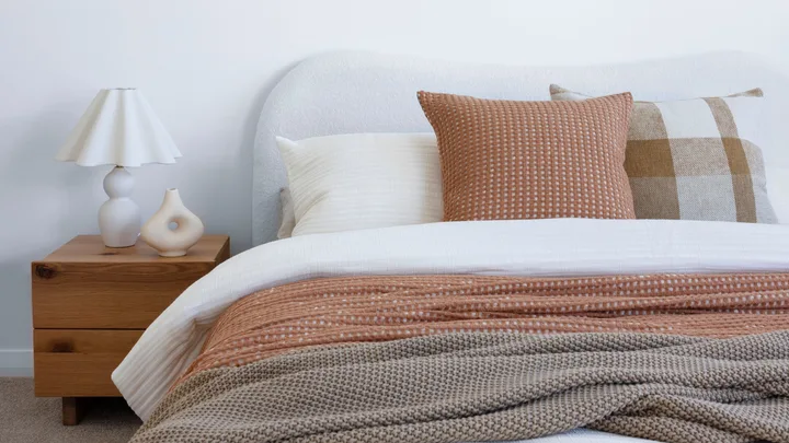 white organic curved bed frame with a white duvet, rust and green blankets and multi-coloured pillows