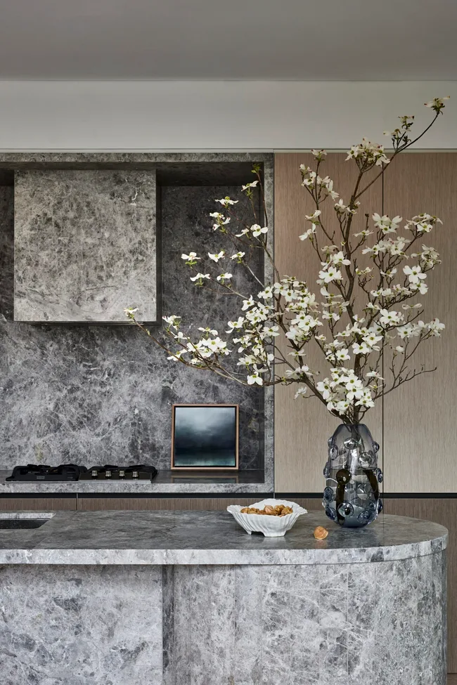 A large island is centred in the kitchen, with grey marble on the top and sides. This marble is also on the splashback, rangehood and benchtop, surrounded by Eveneer joinery.