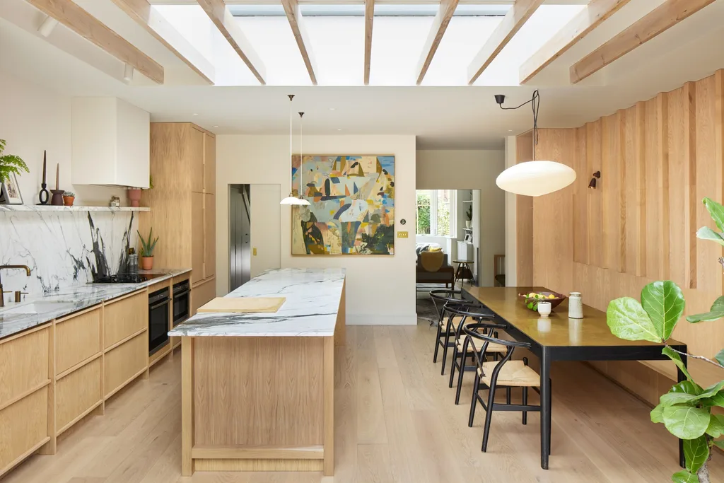 Light timber scandinavian and japanese inspired marble kitchen with an island bench, skylights, a brass dining table, banquette seating and wishbone chairs