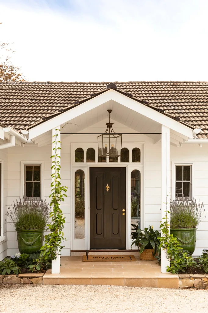 Black front door under white gabled entry with green pots either side