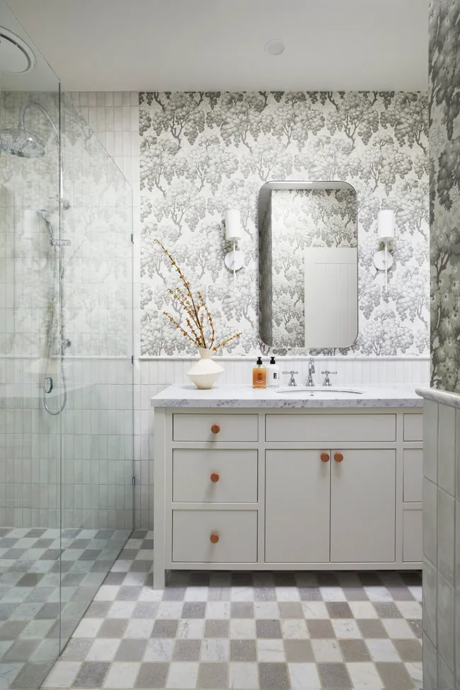 An English country style bathroom with white cabinetry and a marble-topped vanity. A rectangular mirror is placed above this.