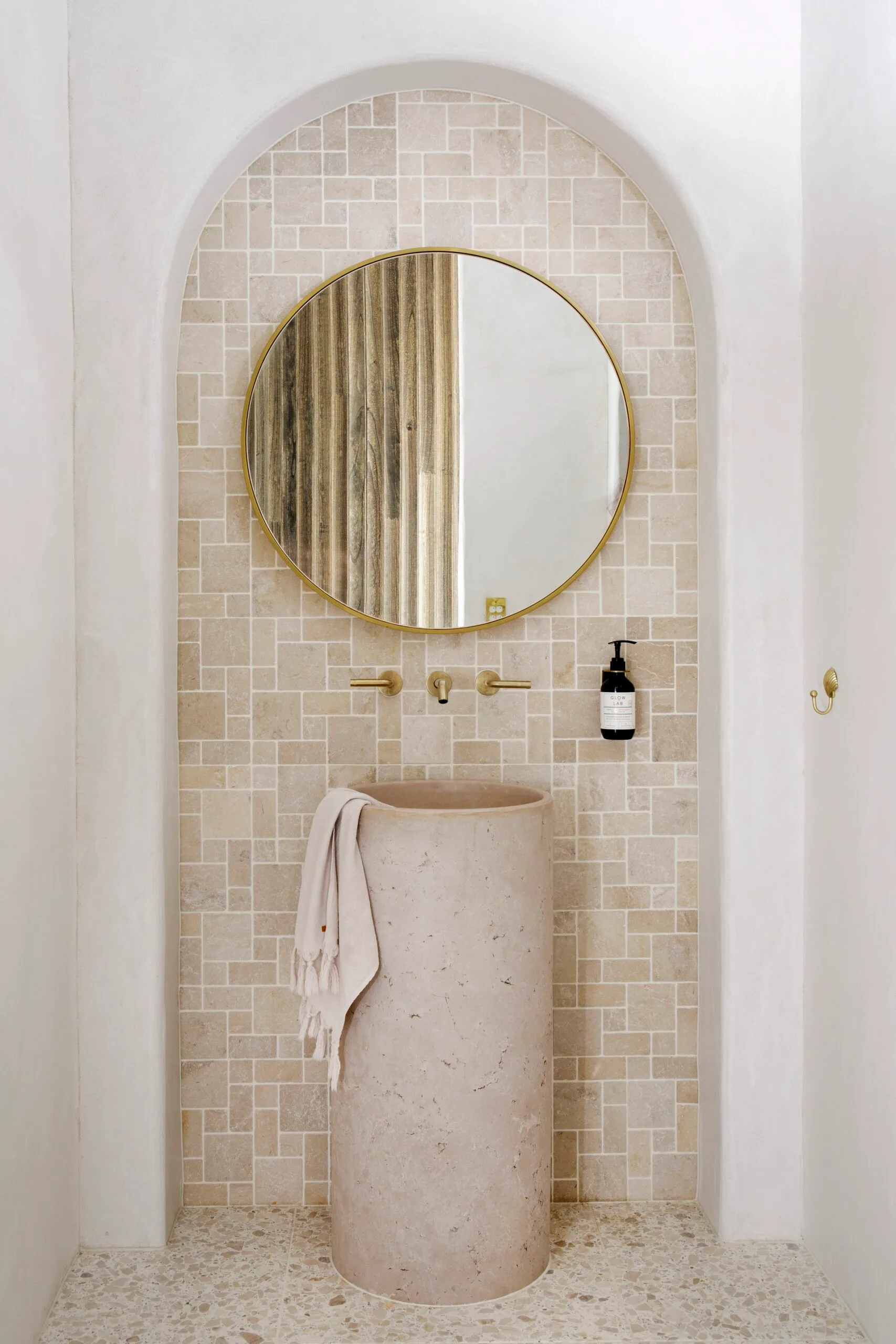 A modern Mediterranean style bathroom vanity with a freestanding basin below a circular mirror.