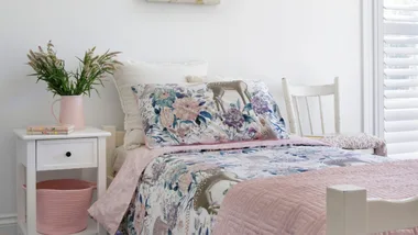 Child's bedroom with floral bedding, pink accents, deer artwork on white wall, and a bedside table with plants.