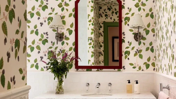 A green bathroom with botanical wallpaper, white tiled wainscoting and green bathroom joinery.