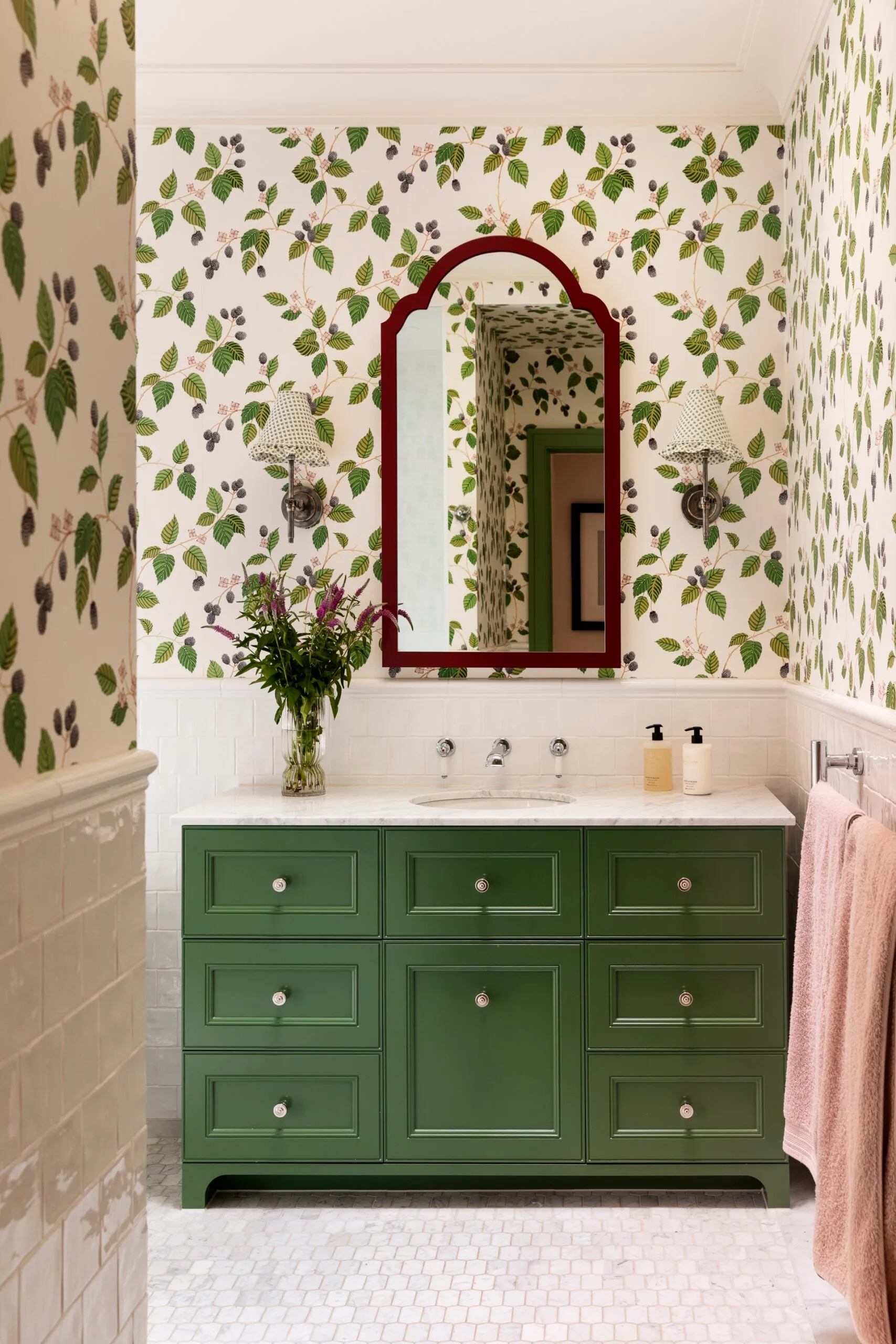 A green bathroom with botanical wallpaper, white tiled wainscoting and green bathroom joinery.