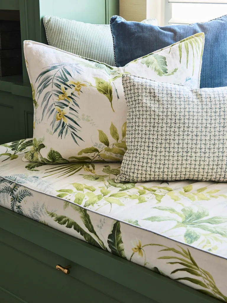 A window seat upholstered in a botanical inspired print with botanical inspired prints also used on the cushions which decorate it. Green joinery is visible beside and underneath the window seat.