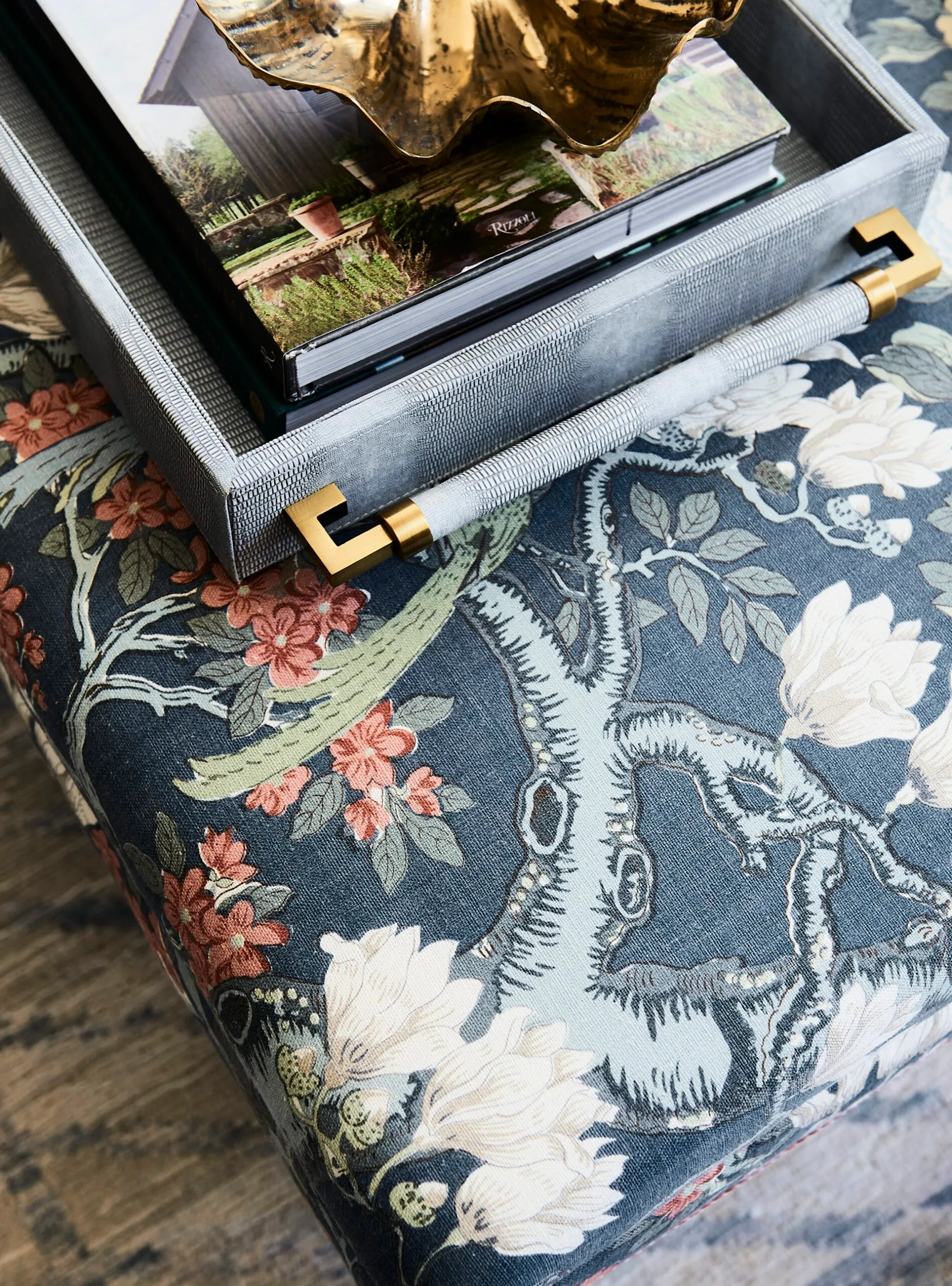 A botanical print on an upholstered ottoman used as a coffee table, in a green and blue lounge room.