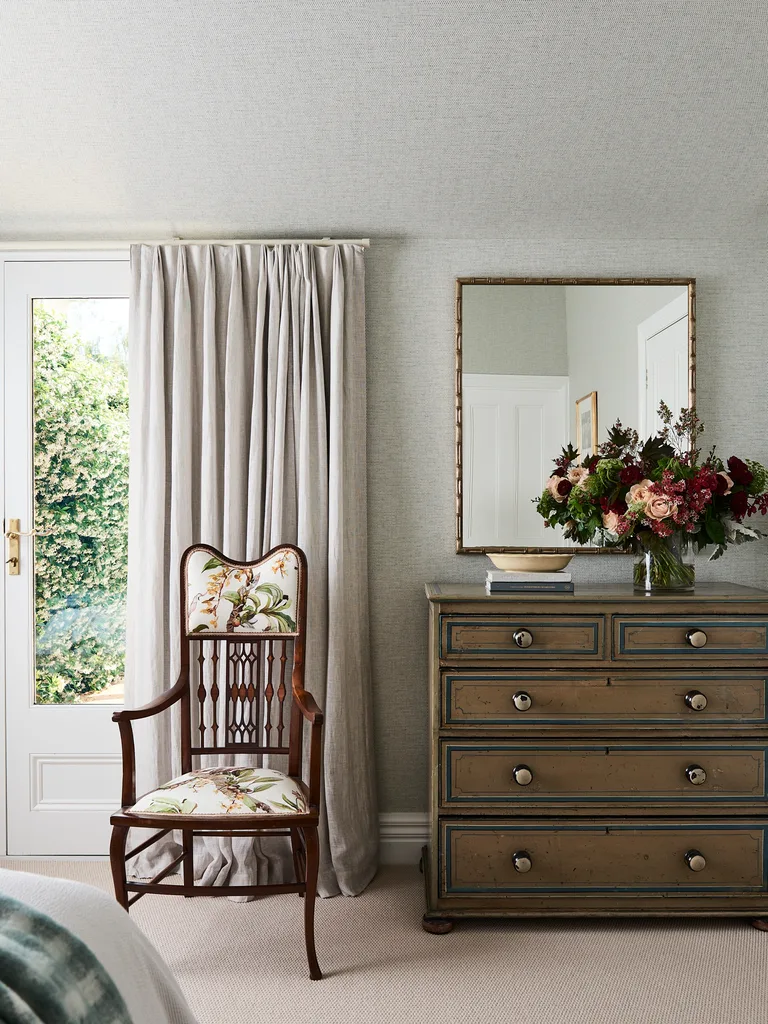 A wooden dresser in a bedoom with a timber chair with botanical patterned upholstery.