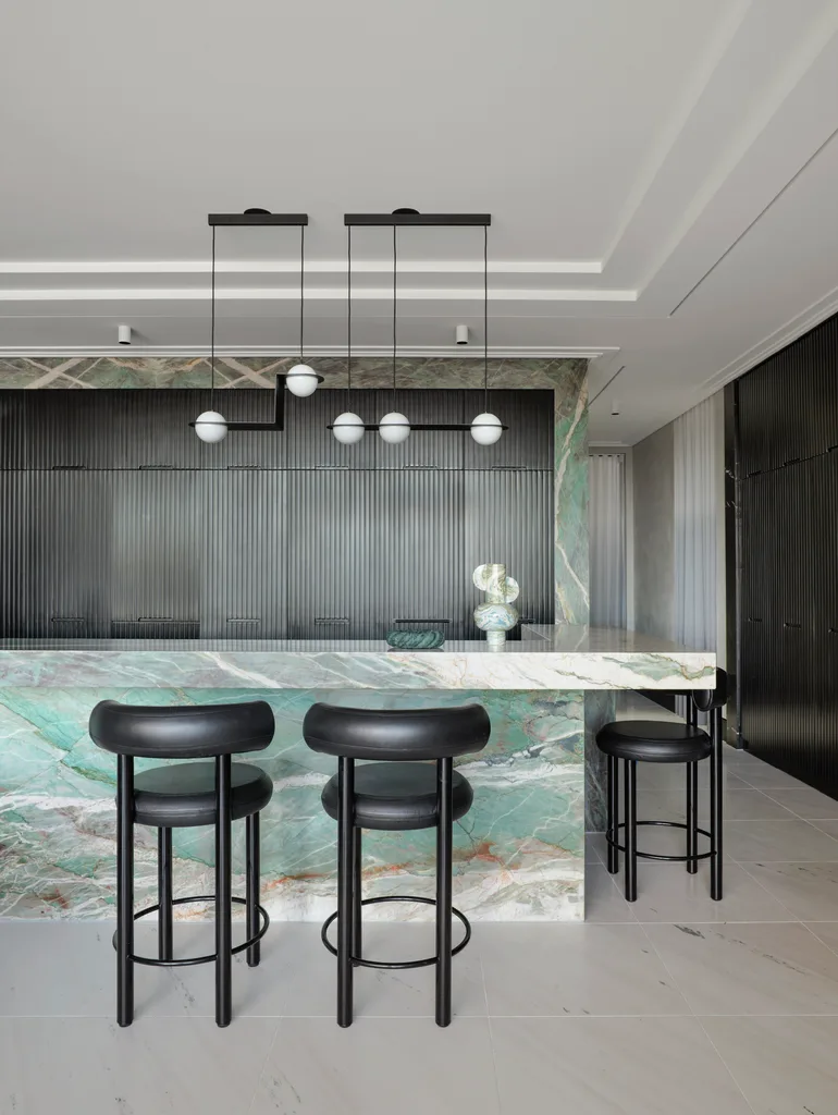 A masculine kitchen design with green marble island and benchtops, black cabinetry and black leather bar stools.