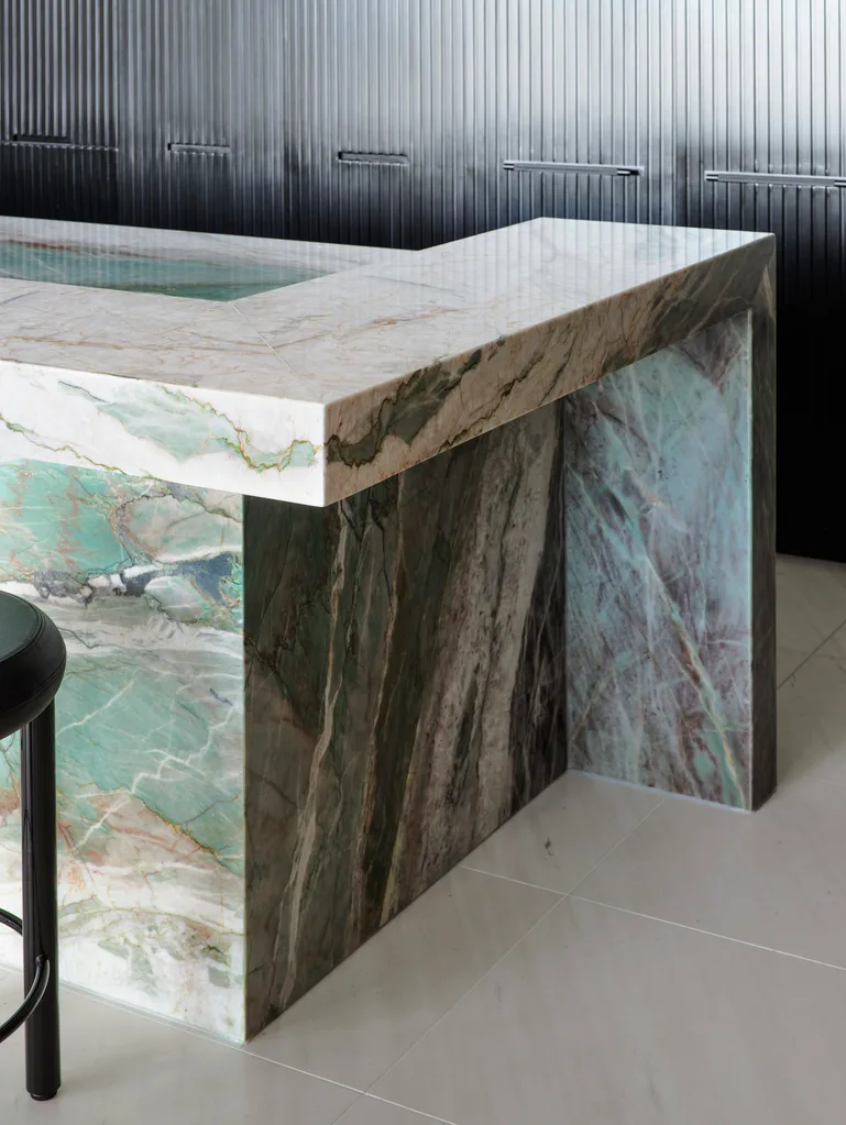 A masculine kitchen design with green marble island and benchtops, black cabinetry and black leather bar stools.