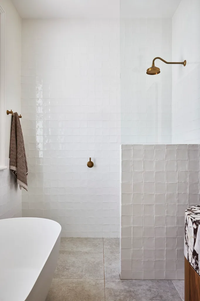 A white bathroom which showcases small bathroom design ideas, such as nib walls to delineate spaces and white tiles that draw the eye upwards to high ceilings.