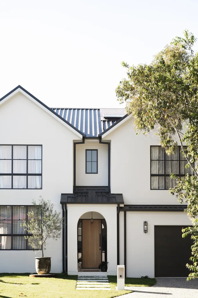 An exterior shot of a white house with black roof and trims, with an archway leading to the front door. The arch is typical of Spanish mission-style.