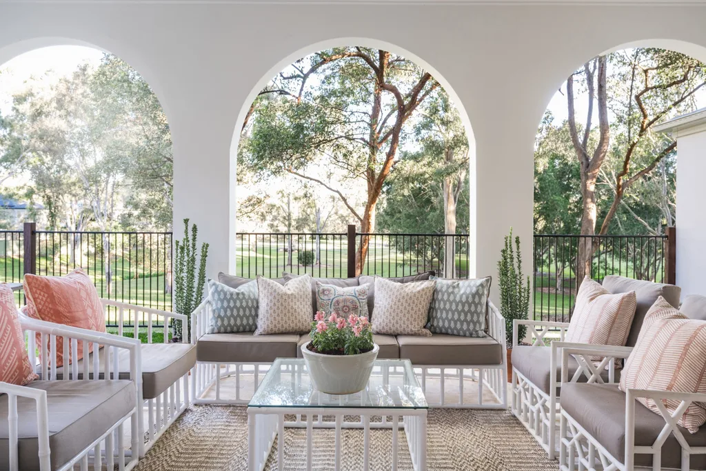 An alfresco living area with furniture that has white frames and grey cushions. Three arches delineate the alfresco area and garden, typical of Spanish mission-style.