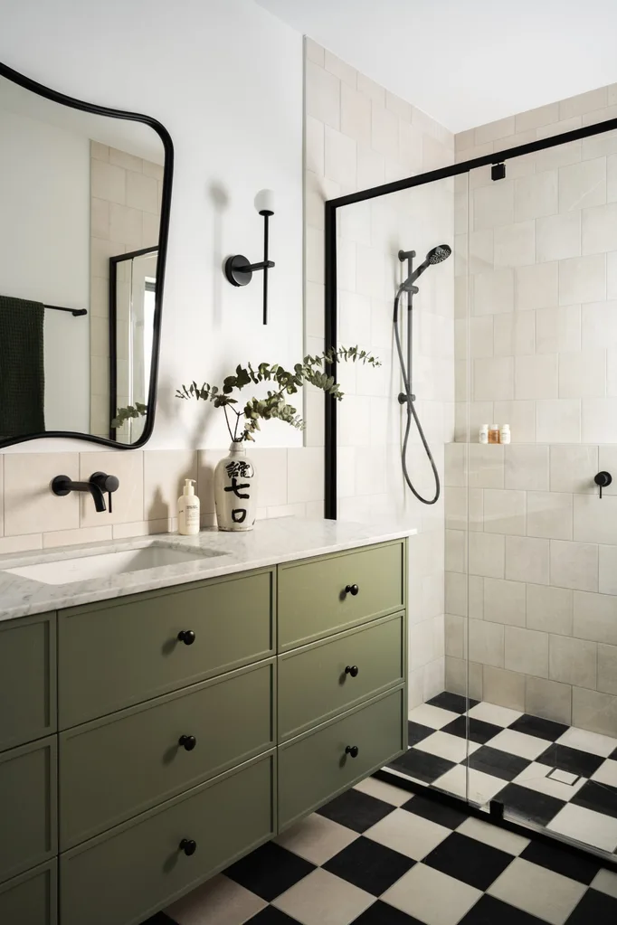 A bathroom with black and white checkerboard tiles and green cabinetry plus a shower to the right.
