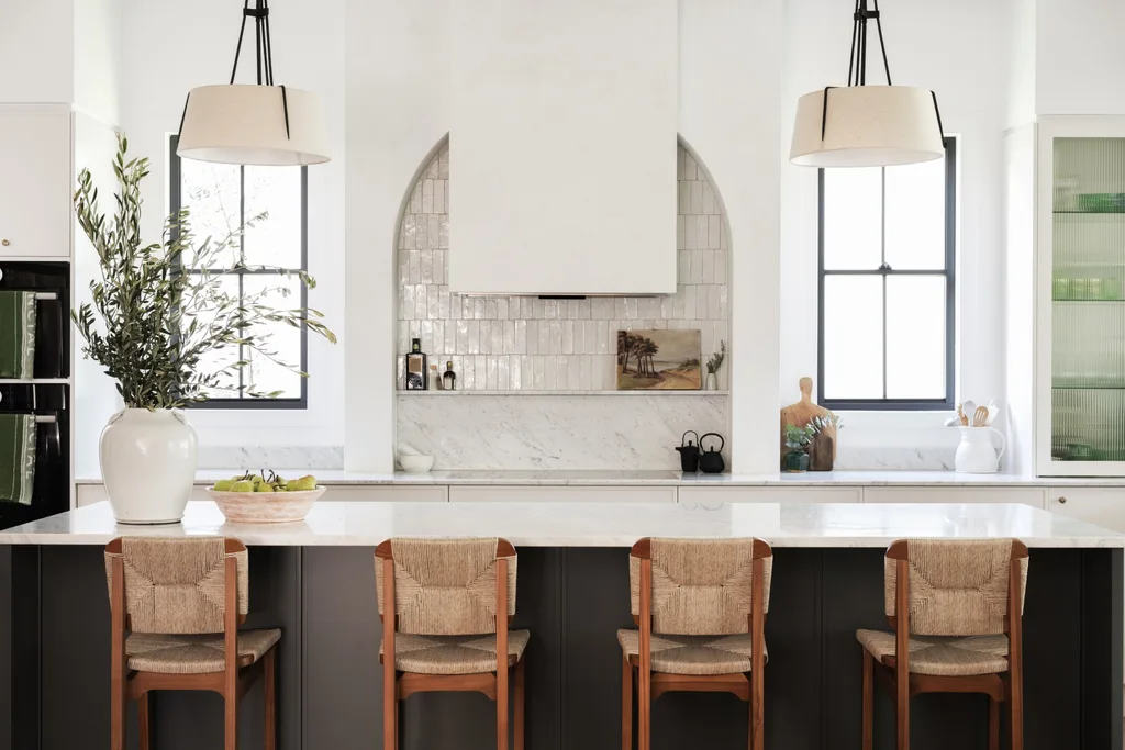 A kitchen with white tiles, a neutral toned marble benchtop and splashback plus a sizable kitchen island which has black panelling on the sides.