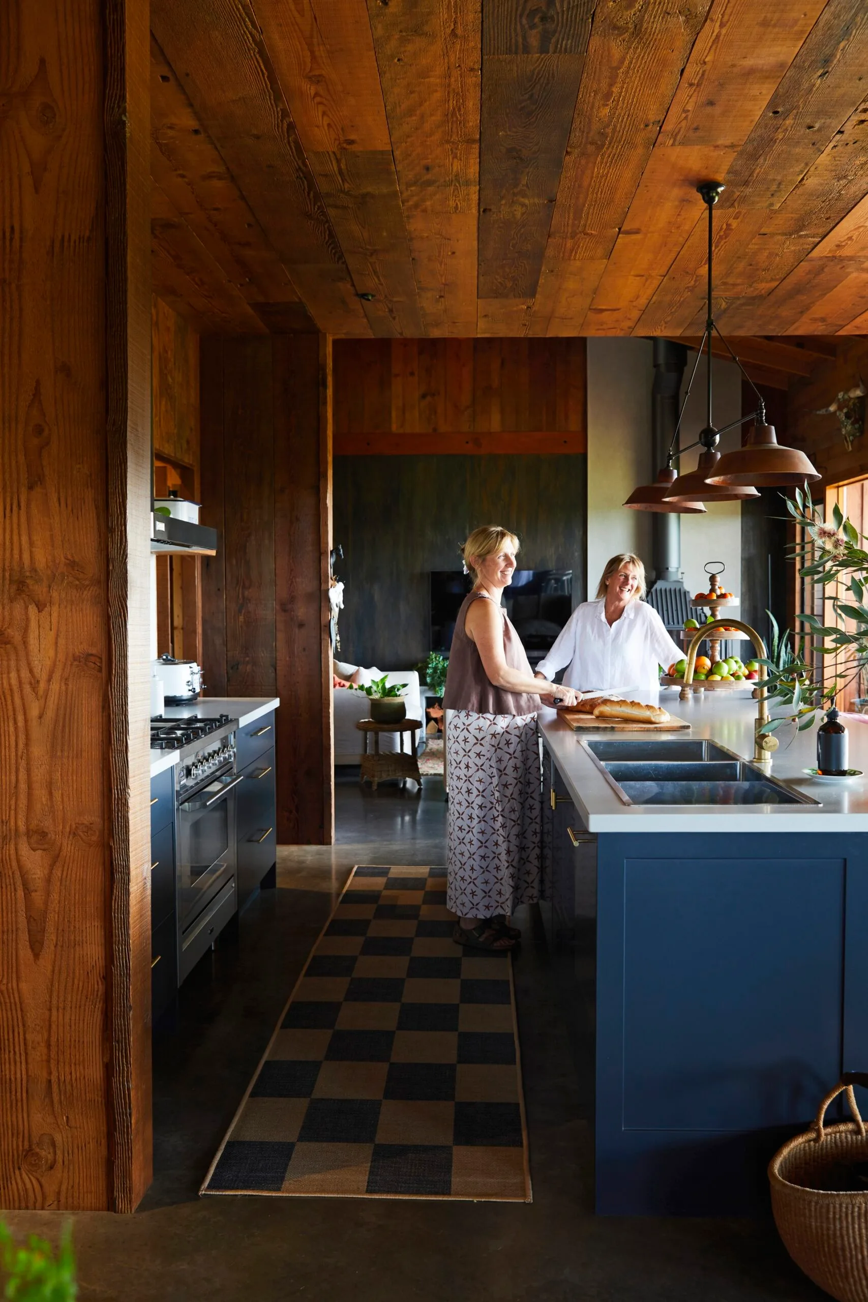 Mother and daughter stand in a timber kitchen with checkerboard rug. 