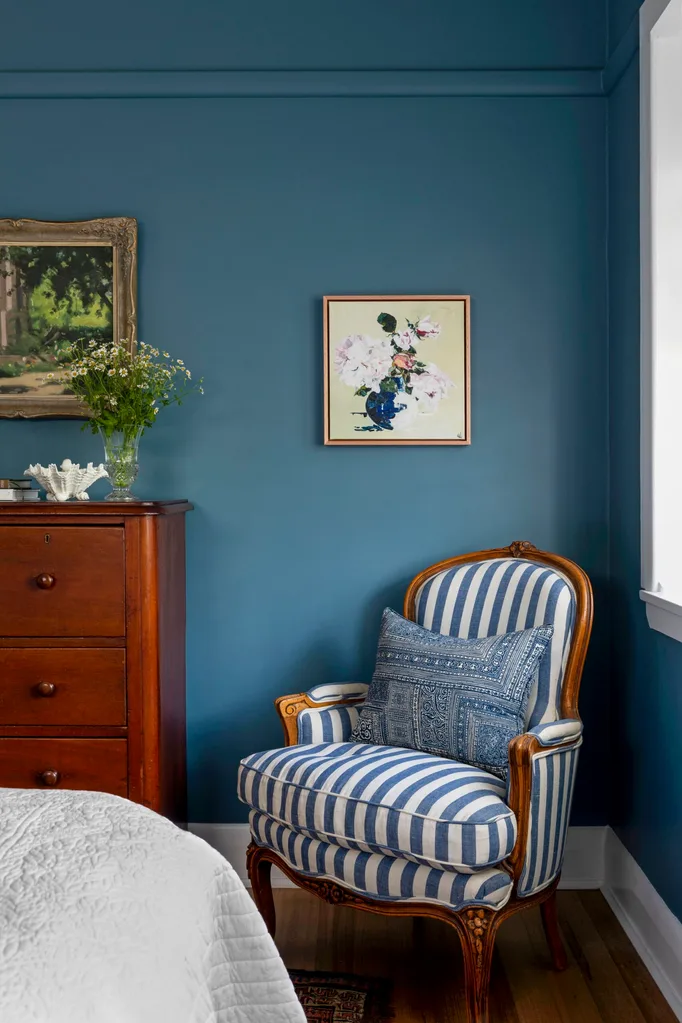 The corner of a bedroom with walls painted blue, a timber set of drawers and a blue and white striped armchair. The palette feels perfect for winter decorating and could inspire winter decorating ideas.