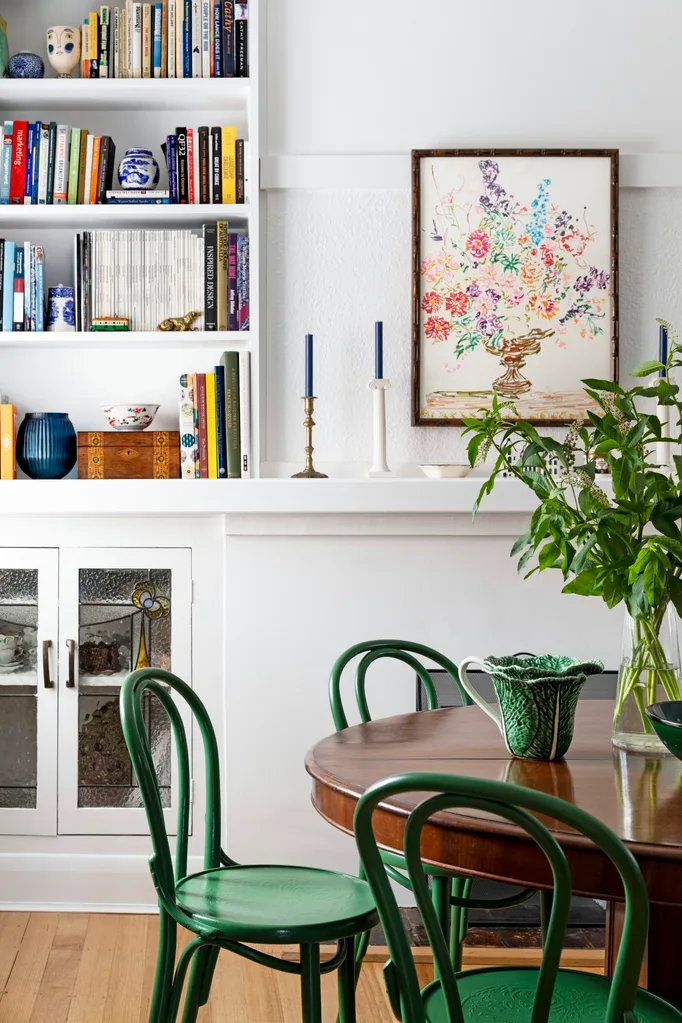 A dining area with round mahogany dining table, green bentwood dining chairs in front of a white wall with built in white cabinetry and bookshelves. The palette feels perfect for winter decorating and could inspire winter decorating ideas.