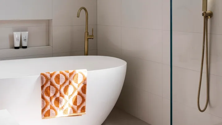 A bright, contmporary bathroom with a freestanding bath and orange patterned towel.