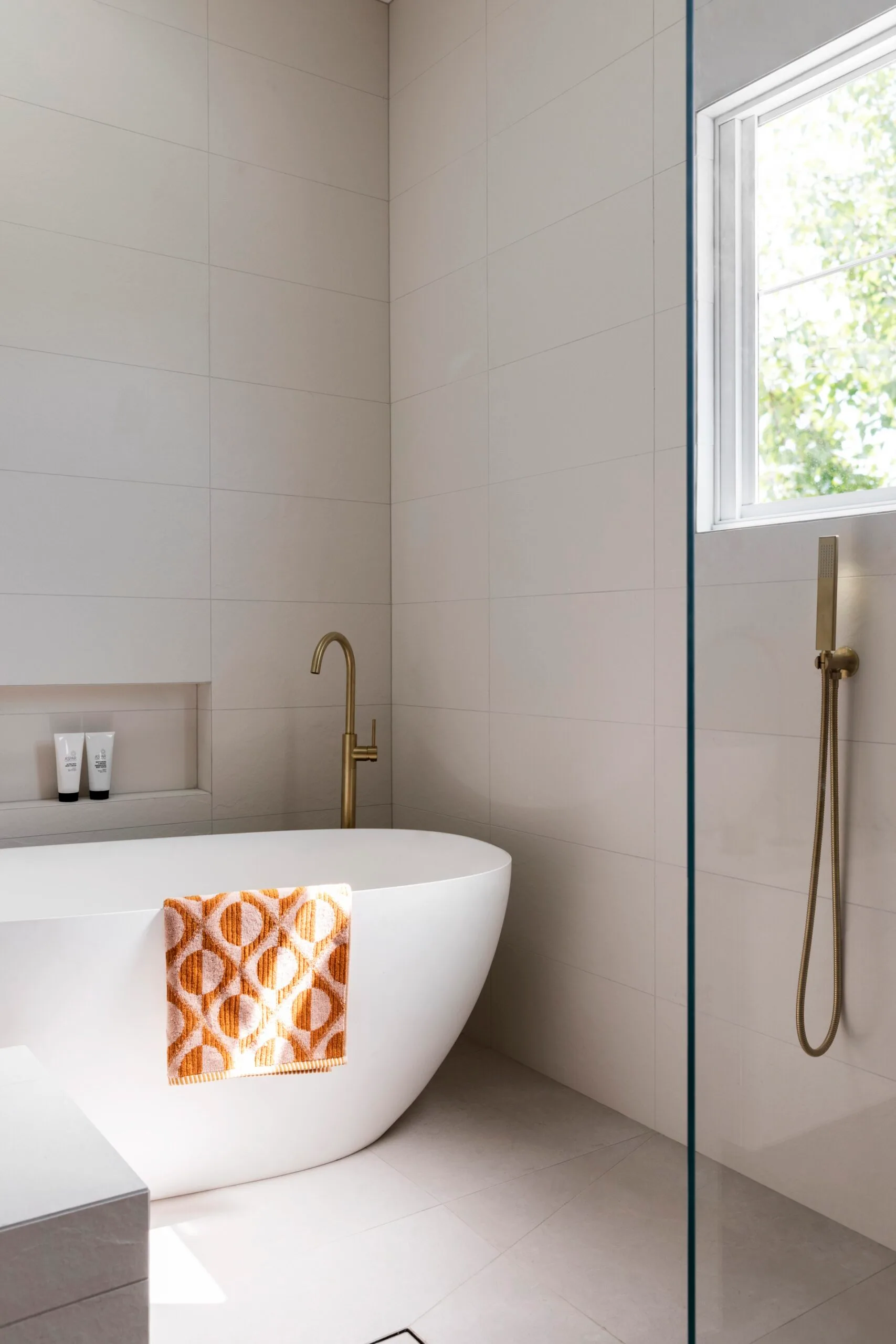 A bright, contmporary bathroom with a freestanding bath and orange patterned towel.