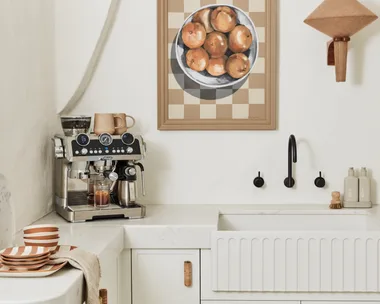 A DeLonghi coffee machine with built in milk steamer and coffee grinder on a white kitchen bench with white cabinetry and white walls.