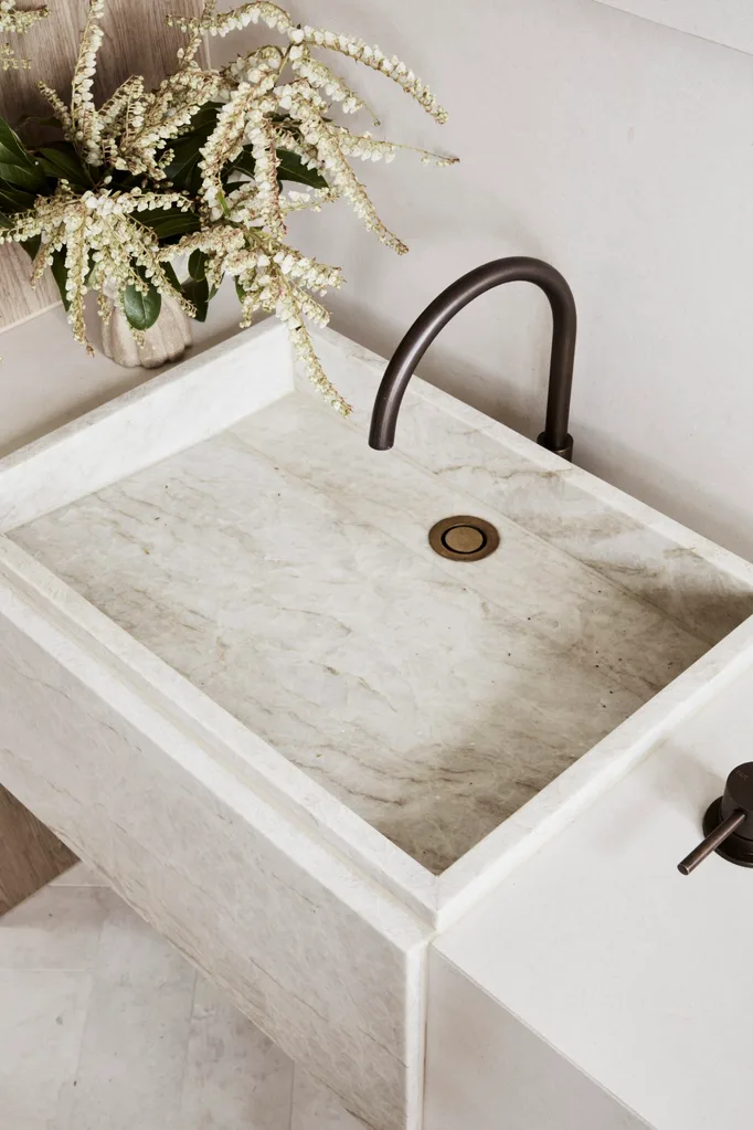 A close up of a square basin made out of stone in a bathroom. Earth tones fit in to the earthy colour palette, with a gooseneck tap in weathered brass organic and honed quartzite for the basins.
