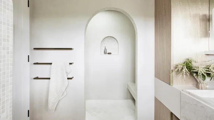 Earth tones fit in to the earthy colour palette in this bathroom. The floor tiles are raw-sawn limestone laid in a herringbone pattern. An arch leads from the vanity area to a sizable shower, complete with a shower bench made from honed quartzite.