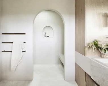 Earth tones fit in to the earthy colour palette in this bathroom. The floor tiles are raw-sawn limestone laid in a herringbone pattern. An arch leads from the vanity area to a sizable shower, complete with a shower bench made from honed quartzite.