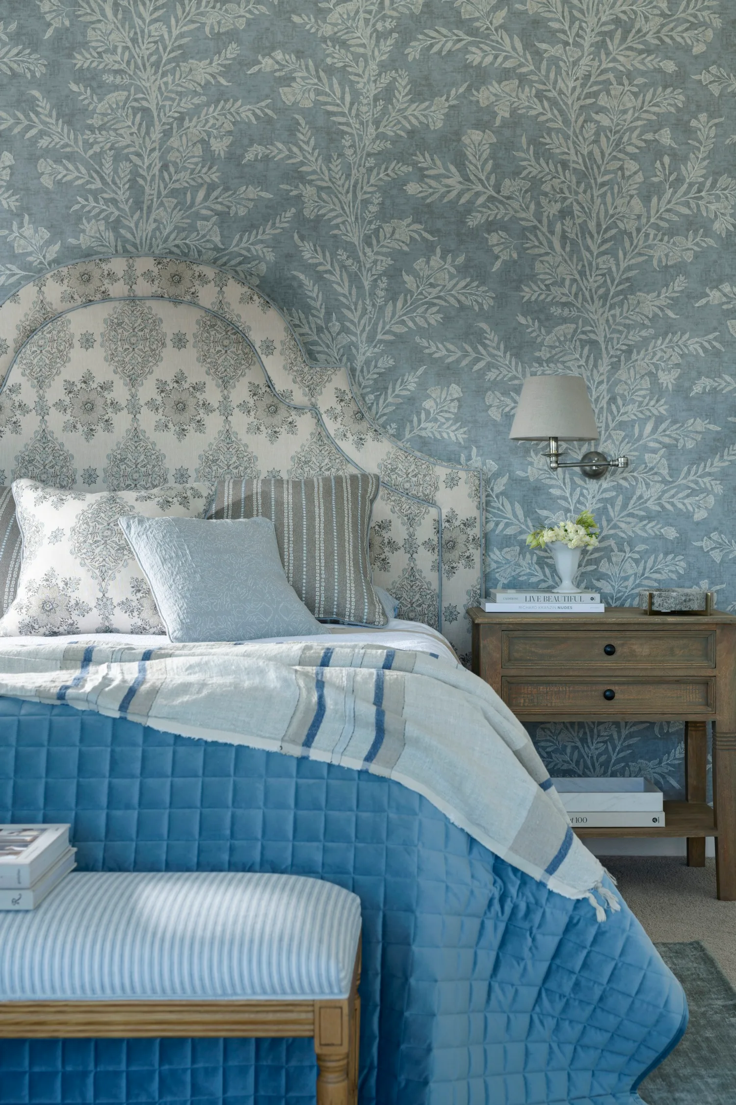 Bedroom with blue patterned wallpaper and blue bedding with lamp on side table