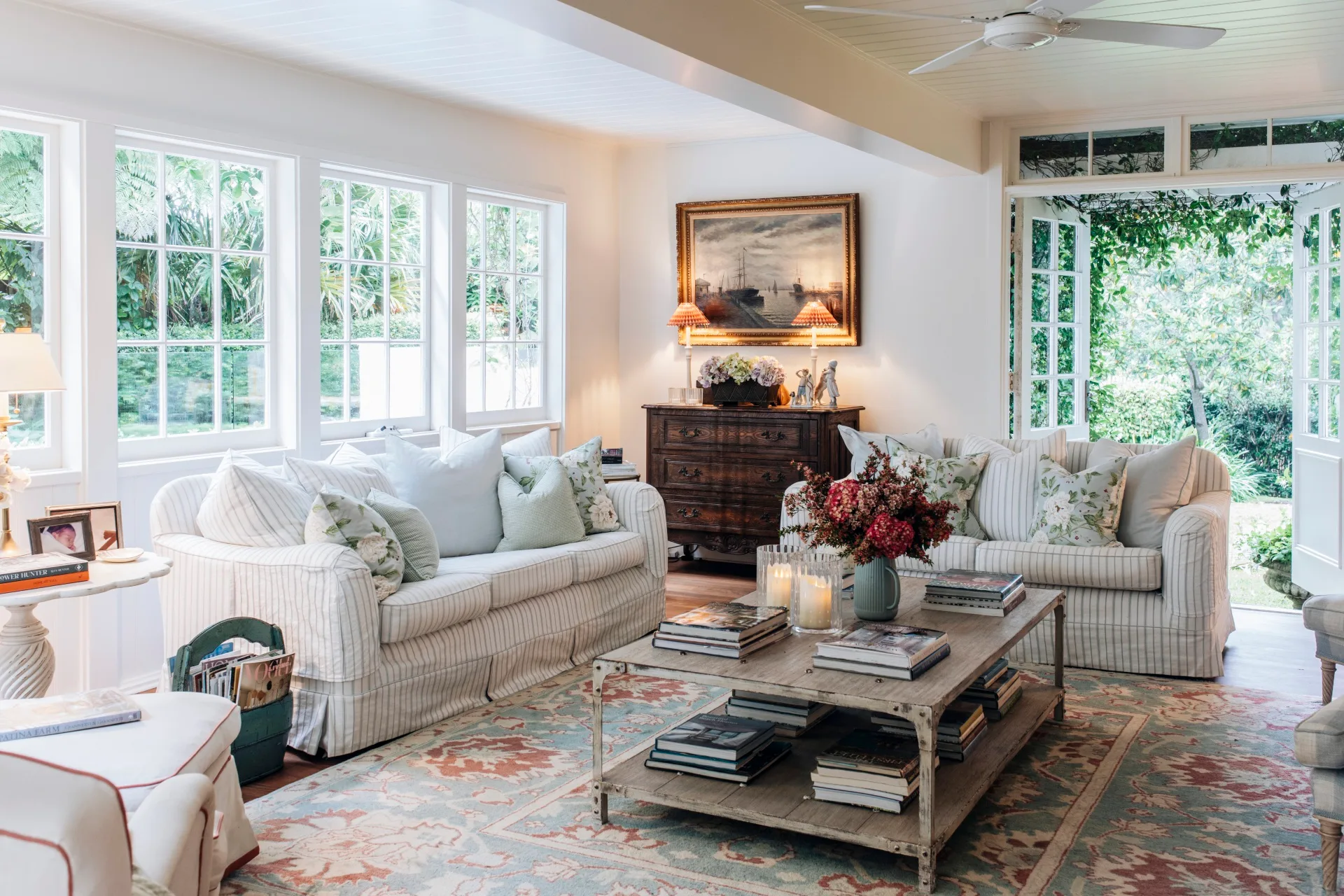 The light-filled living room of a Nantucket style home in Palm Beach, with striped couches and picture windows. 