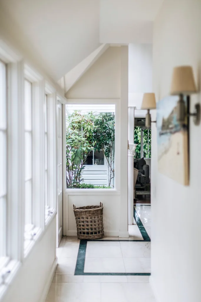 A tiled hallway with windows and wall sconces in a Nantucket style home in Palm Beach.