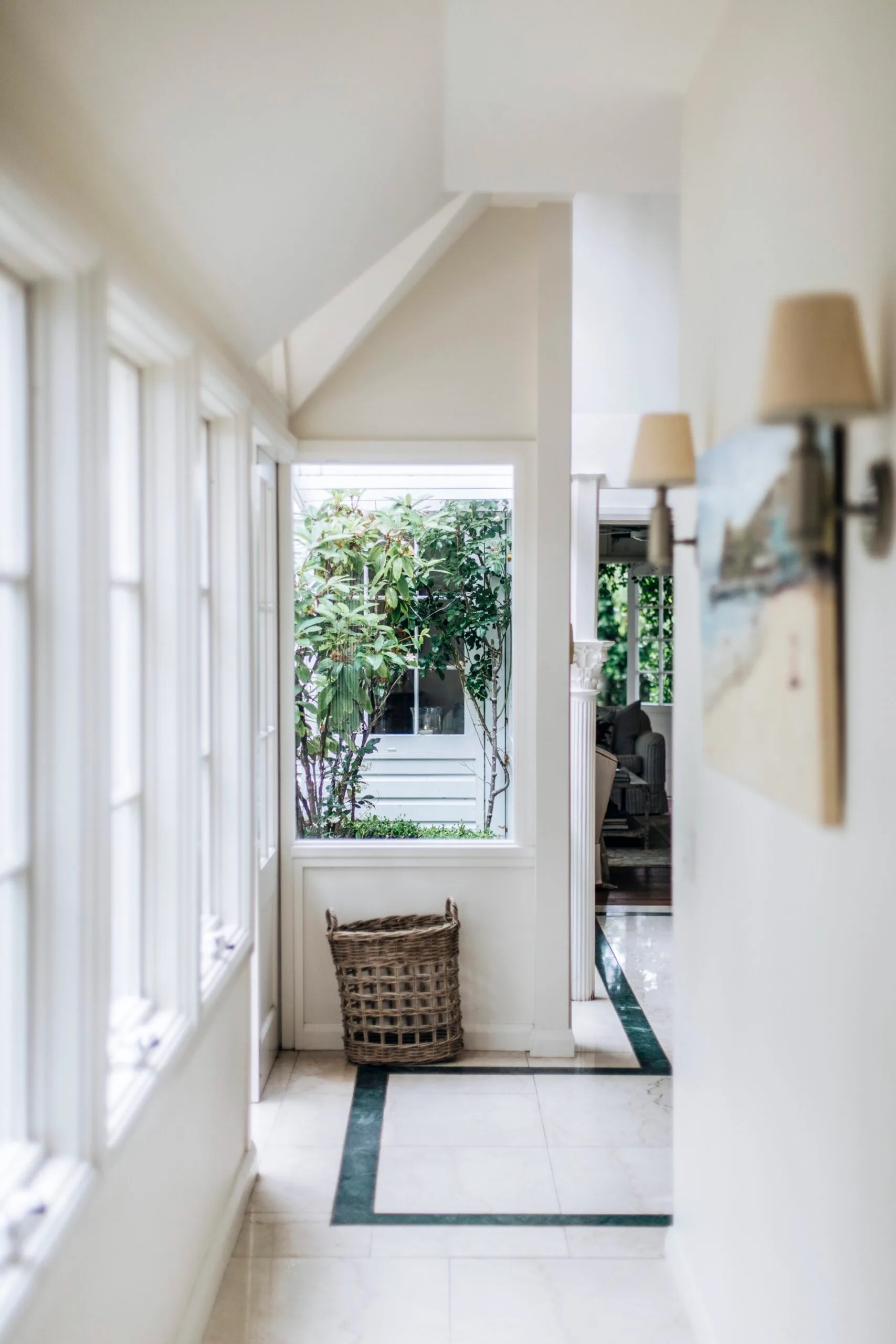 A tiled hallway with windows and wall sconces in a Nantucket style home in Palm Beach. 