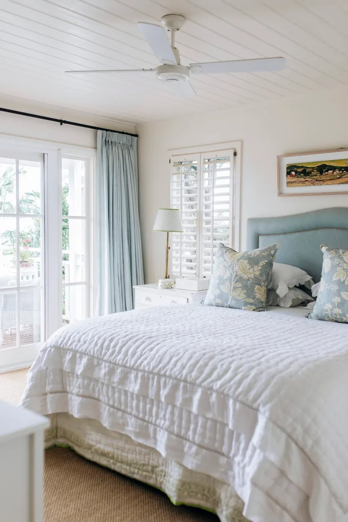 A bedroom furnished in soft blues, including a bed head, patterned cushions and blue curtains.