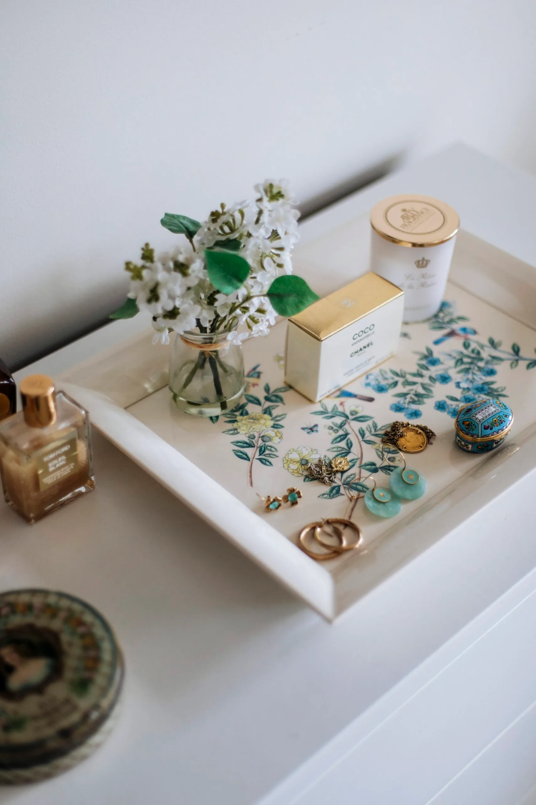 A decorative tray with jewellery, candles and a vase of flowers. 