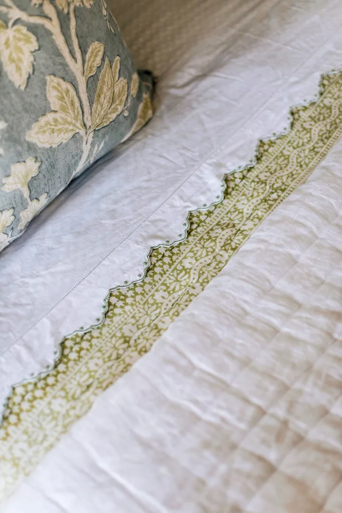 A green patterned bedspread and soft blue cushion.