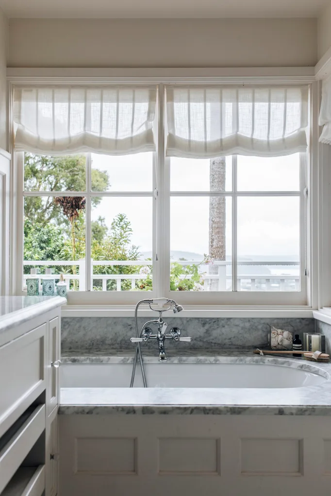 A grey-veined marble bath and striped linen roman blinds.