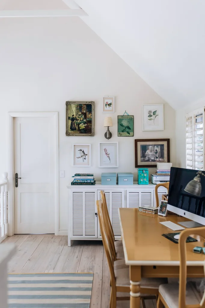 A wooden desk with art on the wall in the study of a Nantucket inspired home.